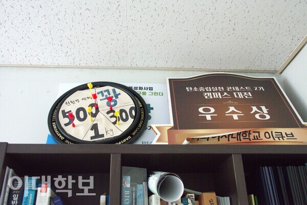 책꽂이 위에 친환경 세제 증정 게임에 사용된 다트판과 ‘탄소중립실천 컨테스트 2기 캠퍼스 대전’에서 받은 우수상 팻말이 놓여 있다. 정영인 사진기자