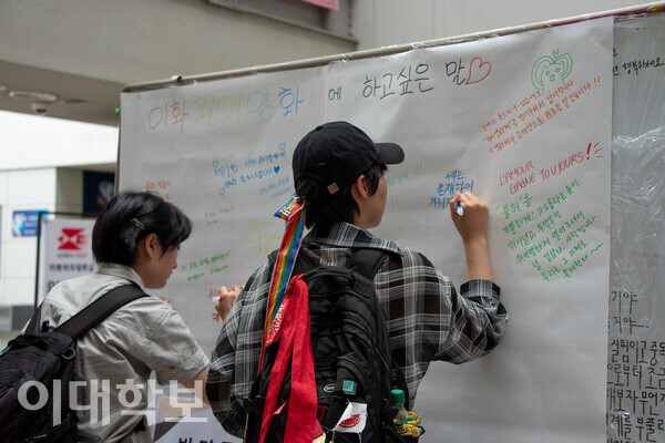 학문관 1층에 마련된 이화퀴어영화제 방명록에 한 이화인이 “우리는 존재하며 지워지지 않는다”라는 메시지를 남기고 있다. 진유경 사진기자