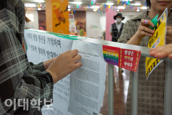 이화퀴어영화제 참가자들이 아트하우스 모모 앞 난간에 퀴어영화제 반대 입장을 규탄하는 대자보와 퀴어와의 연대를 상징하는 스티커들을 붙이고 있다. 출처=이대학보 DB