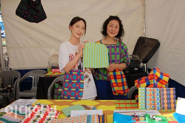 브랜드 ‘오카모카’ 부스의 전민지(공간디자인 전공 석사과정)씨(왼쪽)와 하성옥(장식미술·90년졸)씨가 판매하는 테이블매트를 들고 미소짓고 있다. 대표 하성옥씨는 “오카모카란 색종이 테라피로 패턴을 만드는 생활용품 브랜드”라고 설명했다. 정영인 사진기자