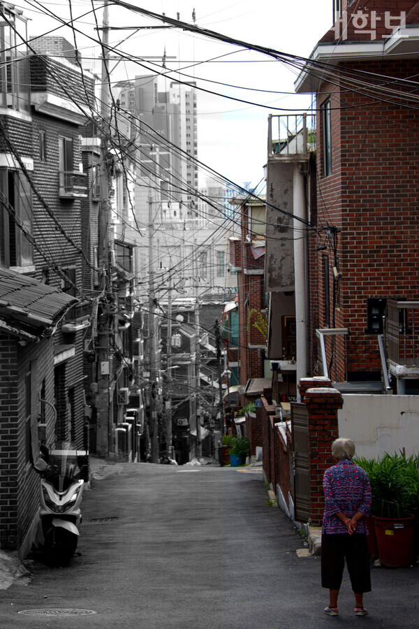 한 주민이 북아현동의 언덕 아래 풍경을 내려다보고 있다. 오래된 빌라 건물들과 재개발된 구역의 아파트의 모습. <strong>정영인 사진기자